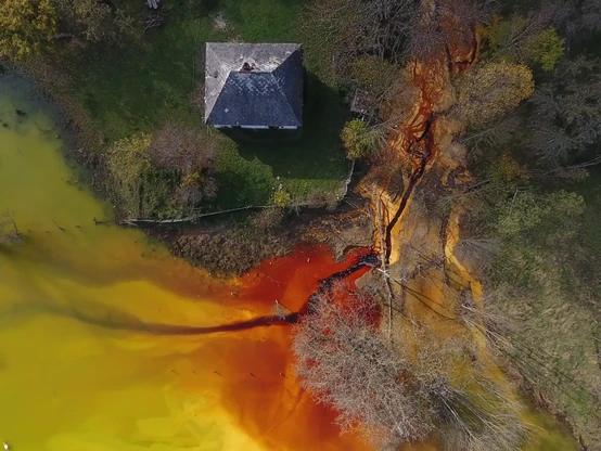 Aerial picture of a house surrounded by red-stained lake used for storing toxic waste.
