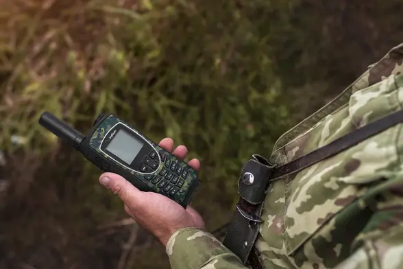 A soldier holding an Iridium 9575 Extreme PTT with Camo Case in their hand. 
Notice it's small width!
The Antenna is not deployed and the device is seemingly off. A soldier holding an Iridium 9575 Extreme PTT with Camo Case in their hand. 
Notice it's small width!
The Antenna is not deployed and the device is seemingly off.