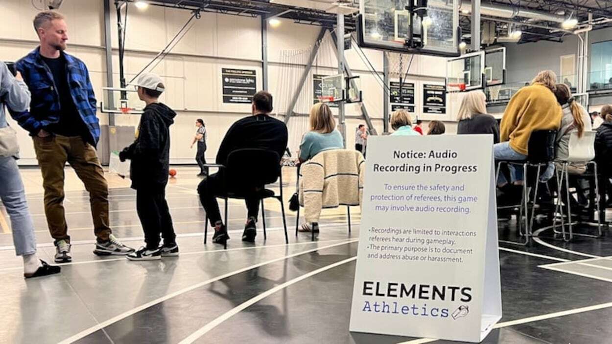 Des spectateurs assistent à un match de basketball, près d'un panneau signalant un enregistrement audio.