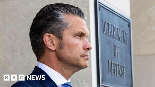 A file photo of Pete Hegseth standing in front of a sign which reads "Department of Defense"