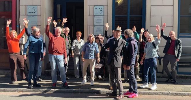 Gruppenbild mit mehreren Personen vor einem Hauseingang in Bremen, die in die Kamera winken.