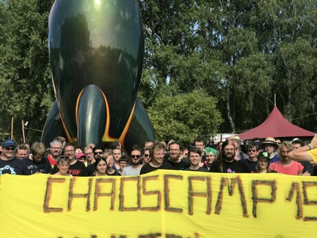 Menschen mit Transpi "Chaoscamp 19" vor der CCC-Rakete, Nahaufnahme