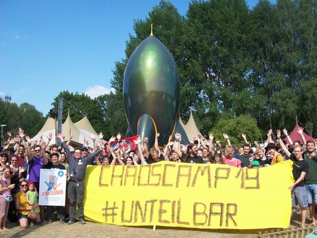 Gruppe von Menschen winken vor CCC-Rakete mit Transpi "Chaoscamp 19 #Unteilbar"