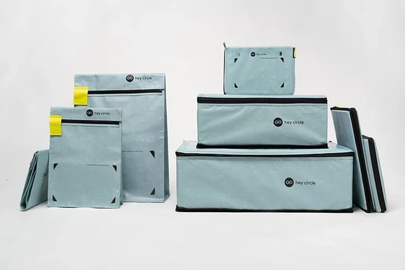 Bild der Mehrwegverpackungen. Links eher klassisch ausschauende Versandtaschen, rechts typische Kartons mit der Besonderheit, dass oben und unten Reißverschlüsse sind, sodass zusammengefaltete Pakete nicht wieder aufgehen