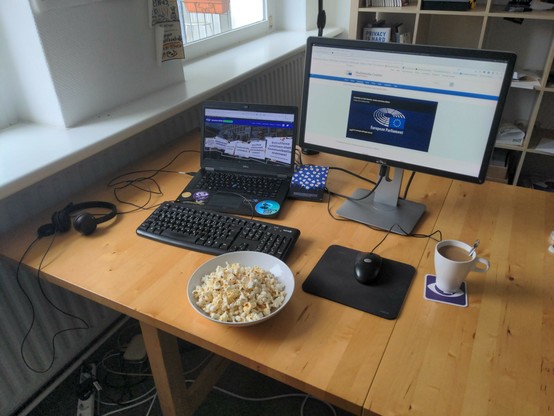 Ein Arbeitsplatz mit Kaffee, Popcorn und einem Livestream aus dem Europäischen Parlament.