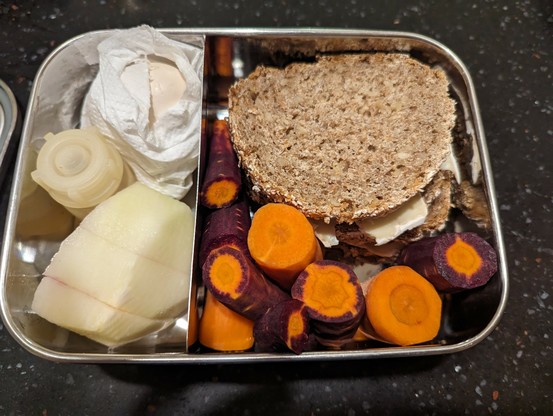 Brotzeitdose aus Metall mit belegten Vollkornbroten, Karotten, Kohlrabi und Ei.