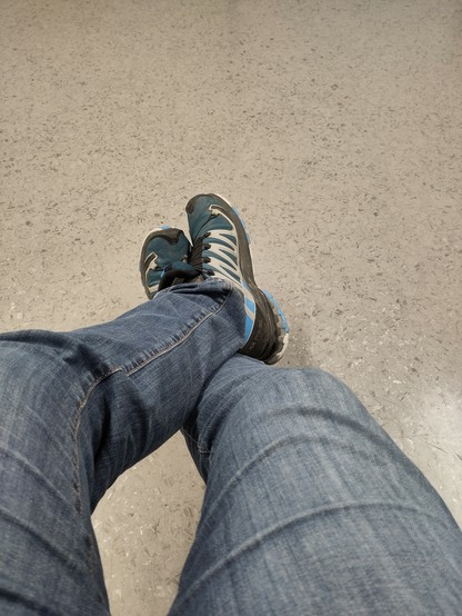 Zu sehen sind meine Beine, das linke ist über das rechte geschlagen. Ich trage blue Jeans. Die Schuhe sind hellblau mit weißen zick-zack Muster an der Seite.