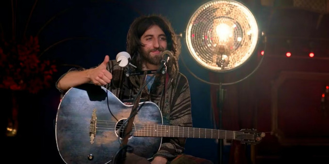 Cam Cole mit Gitarre auf der Bühne bei Ted Lasso vor golden leuchtender Spiegel-Halbglobus-Stehlampe