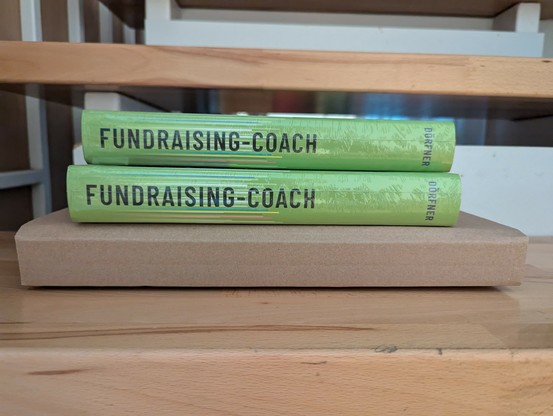 Zwei Bücher Fundraising-Coach liegen foliert auf einen Buchkarton.