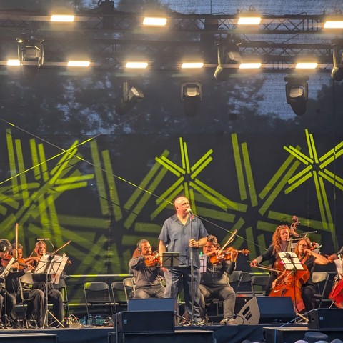 Die Aufnahme zeigt Ronan Harris auf einer Konzertbühne umgeben von Musikern der Philharmie Leipzig. (leider nur Handyqualität) Im Hintergrund hängen große LED - Panels.