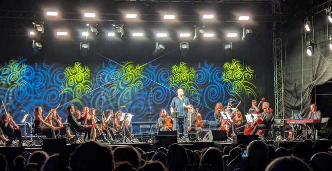 Die Aufnahme zeigt Ronan Harris auf einer Konzertbühne umgeben von Musikern der Philharmie Leipzig. (leider nur Handyqualität) Im Hintergrund hängen große LED - Panels - im Vordergrund das halb im Schatten befindliche Publikum. 