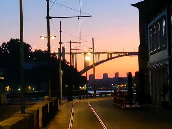 The Douro bridge in Porto during sunset, historic tram tracks some buildings and lots of lampposts and overhead wires.