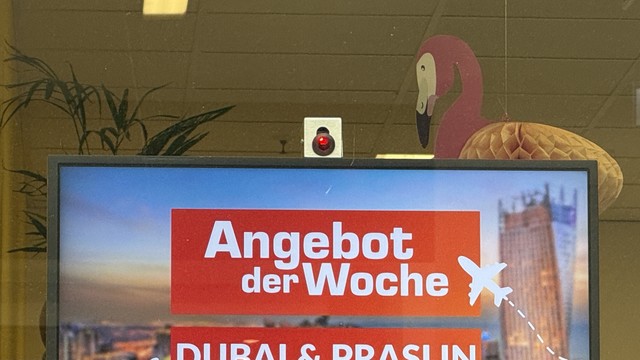 Auf dem Bild sieht man ein digitales Werbedisplay mit der Aufschrift:

„Angebot der Woche – DUBAI & PRASLIN“ (letzteres vermutlich ein Tippfehler für Praslin, eine Seychellen-Insel).

Auffällig ist jedoch etwas anderes:
Über dem Bildschirm ist eine kleine Kamera mit rot leuchtender LED montiert – ein Hinweis darauf, dass hier möglicherweise eine Zuschauer*innen-Erfassung oder sogar Gesichtserkennung erfolgt.

Das könnte z.B. genutzt werden für:
	•	Besucher*innen-Zählung
	•	Blickrichtungserkennung (um zu messen, ob jemand die Werbung ansieht)
	•	Alters- oder Geschlechtsschätzung (z. B. zur Zielgruppenanalyse)

Datenschutzrechtlich ist so etwas nur erlaubt, wenn:
	•	klar und deutlich darauf hingewiesen wird
	•	keine biometrischen Daten gespeichert werden
	•	und die Zweckbindung nachvollziehbar ist

Ein solcher Hinweis ist auf dem Bild nicht erkennbar – das kann problematisch sein. Werbebildschirme mit versteckter Kamera sind oft rechtlich fragwürdig und können als heimliche Beobachtung gewertet werden (§ 6b BDSG / Art. 5 DSGVO).