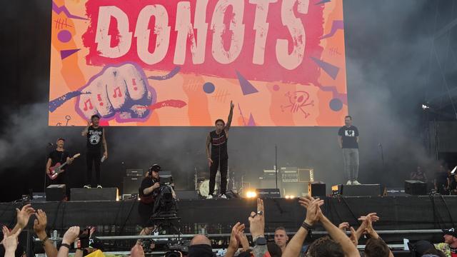 Ein Foto der Bühne. Im Vordergrund erhobene Hände, größtenteils klatschend. Im Hintergrund der Schriftzug "DONOTS". Dazwischen die vom Jubel vergriffene Band. 