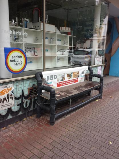Eine Sitzbank aus schwarzen Abflussrohren vor einem Sanitärstudio