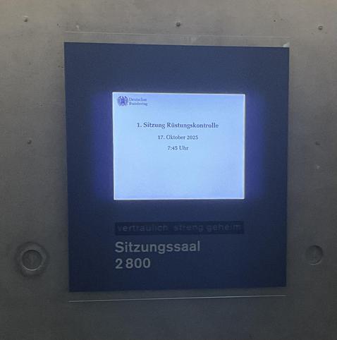 Foto des Bildschirms vor dem Sitzungssaal 2800 mit der Anzeige: „1. Sitzung Rüstungskontrolle.“