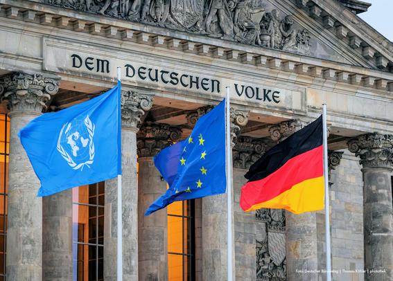 Vor dem Deutschen Bundestag wehen die Fahnen der Vereinten Nationen, der Europäischen Union und Deutschlands.