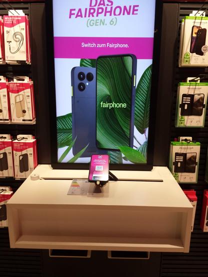 Ein Fairphone 6 im Telekom-Shop. Vorne das Demo-Modell, das man ausprobieren kann und hinten dran ein eine relativ große Werbung von dem Fairphone.