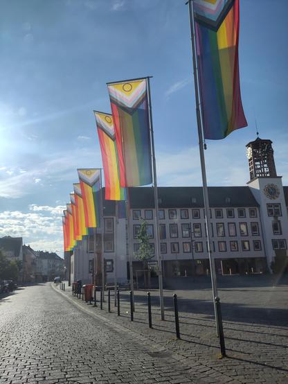 LGBTQ Regenbogen Fahnen am Rathausplatz in Worms. Im Hintergrund das Rathaus bei Sonnenschein und blauem Himmel