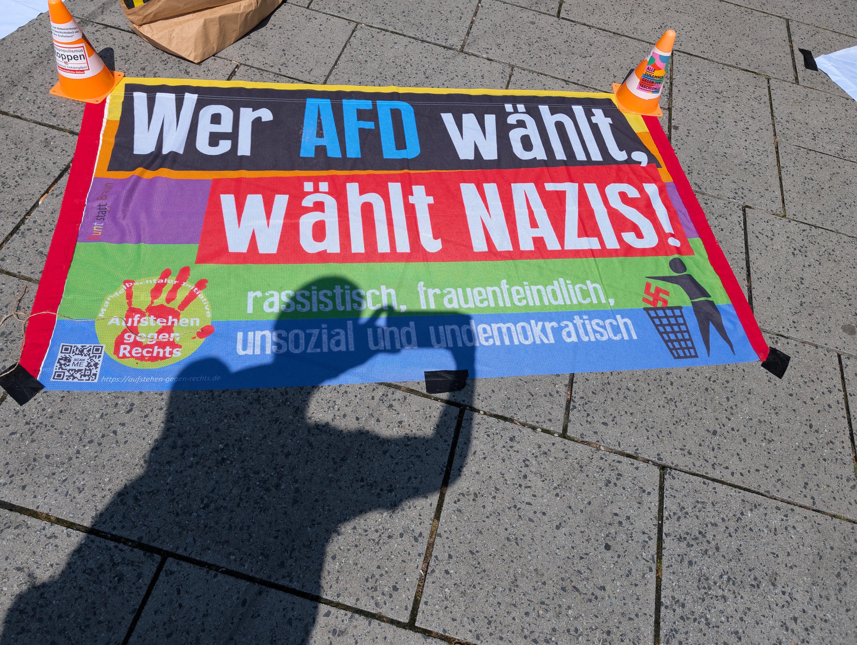Auf dem Boden befestige Fahne mit dem Aufdruck: Aufstehen gegen rechts. Wer AfD wähl, wählt Nazis. Rassistisch, frauenfeindlich, unsozial und undemokratisch.